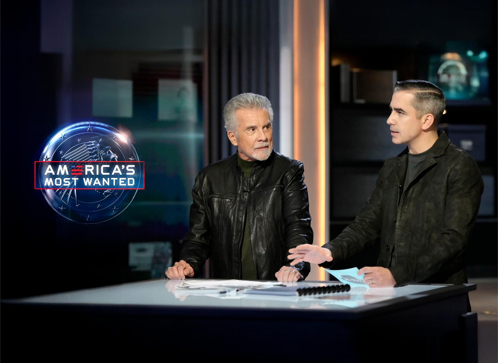 john and callahan walsh stand behind desk on amw set