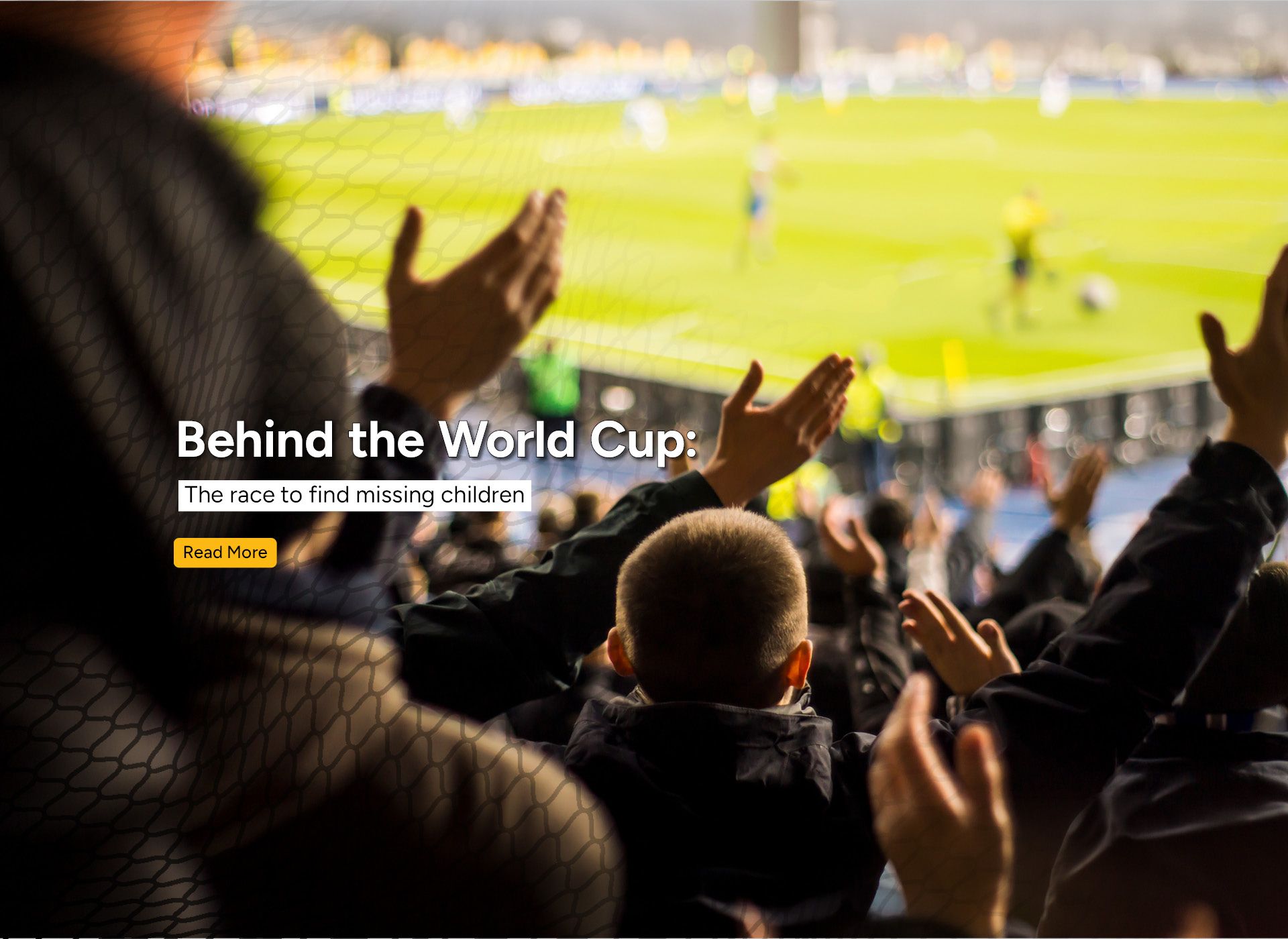 fans, including a small child, clap as a soccer match is going on in the background 